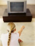 rear view of a girl pointing remote to a&nbsp;television